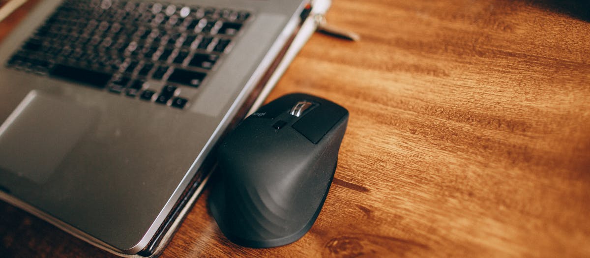 A wireless mouse and laptop placed on a polished wooden desk, perfect for office and remote work setup.